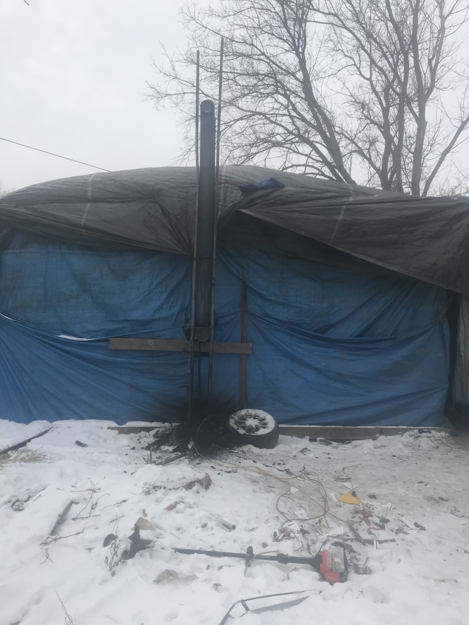 A house trailer, with several tarps snuggly attached, sitting in a snowy field.